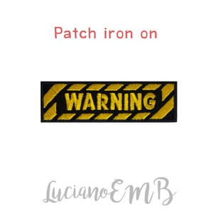 Pode incluir: Um remendo de ferro amarelo e preto com a palavra "WARNING" em letras pretas.