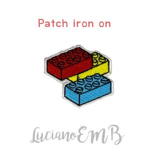 May include: Embroidered patch featuring three colorful toy building blocks in red, yellow, and blue. The text "Patch iron on" is above the blocks. The artist's signature, "Luciano EMB", is below the blocks.