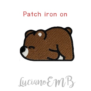 Può includere: Toppa da stirare con un orso marrone che dorme su un fianco. L'orso ha il naso bianco e un occhio chiuso.
