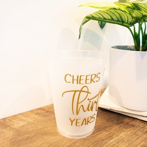 K&ouml;nnte beinhalten: Ein gefrosteter Plastikbecher mit dem Text "Cheers to Thirty Years" in goldenen Buchstaben.