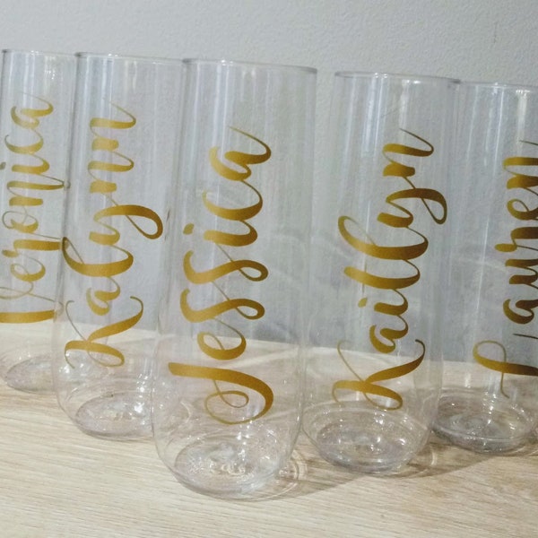 May include: Five clear plastic champagne flutes with gold lettering. The names on the flutes are Veronica, Kaitlyn, Jessica, Kaitlyn, and Lauren.