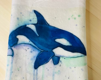 May include: A white plush throw blanket with a watercolor illustration of an orca whale swimming in a blue and green ocean. The orca is black and white with a white patch on its back.