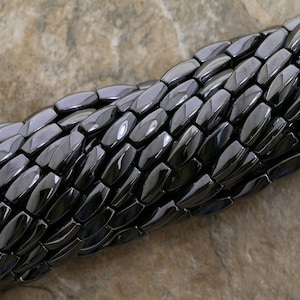 Peut inclure: Un brin de perles d'hématite noire, chaque perle est facetée et de forme rectangulaire.