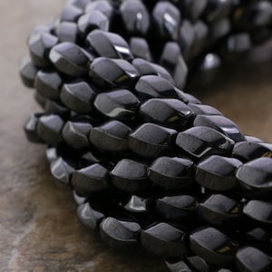 May include: A close-up of a strand of black faceted hematite beads. The beads are arranged in a circular pattern, creating a textured and geometric look.