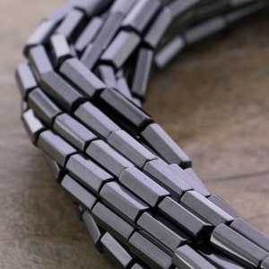 May include: A strand of dark gray, faceted, hexagonal beads. The beads are arranged in a circular pattern, with the ends of the strand overlapping.