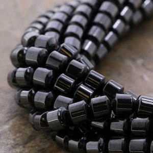 May include: A close-up of a strand of black hematite beads. The beads are round and have a smooth, polished finish. They are arranged in a spiral pattern.