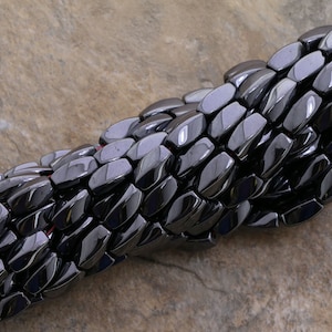 Peut inclure: Un brin de perles d'hématite noire, chaque perle est facetée et de forme rectangulaire.