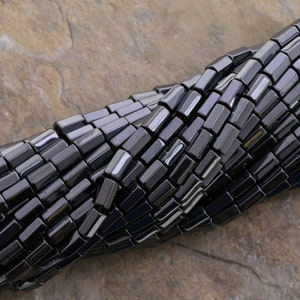 May include: A strand of black hematite beads, each bead is a rectangular prism shape.