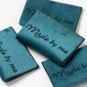 May include: Four teal blue fabric labels with black stitching and the text "Made by me" embroidered in black thread.