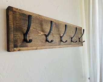 May include: A rustic wooden coat rack with five black metal hooks. The rack is stained a dark brown color and has a natural wood grain.