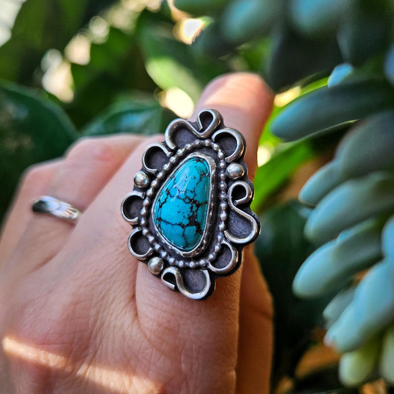 Op de afbeelding: Een turquoise ring met een zilveren zetting. De ring heeft een traanvormige turquoise steen met een zilveren filigraanontwerp eromheen.