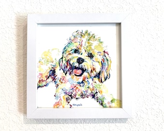 Könnte beinhalten: Ein Aquarellbild eines weißen Hundes mit bunten Akzenten. Der Hund schaut den Betrachter direkt an, mit herausgestreckter Zunge. Das Bild ist in einem weißen Rahmen gerahmt.