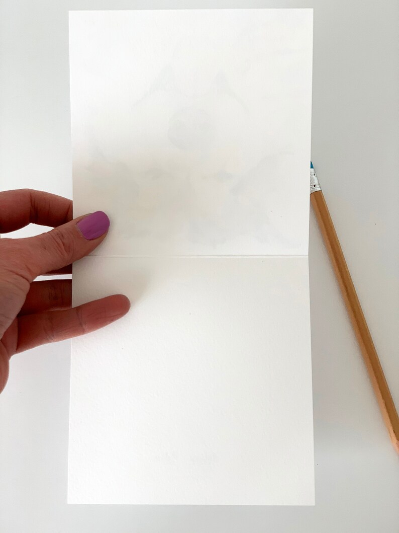 K&ouml;nnte beinhalten: Eine leere wei&szlig;e Karte mit leicht strukturierter Oberfl&auml;che. Die Karte ist in der Mitte gefaltet und wird von einer Hand gehalten.