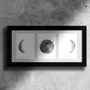 May include: A black framed print with three images of the moon in different phases. The moon is depicted in a black and white watercolor style.
