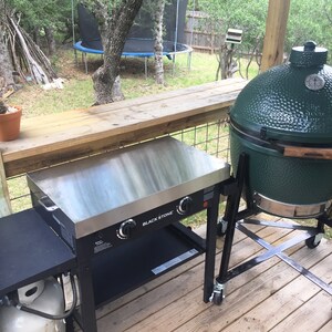 May include: A black and silver outdoor grill with a black propane tank and a green Big Green Egg grill on a wooden deck.