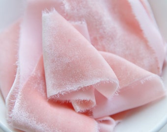 Puede incluir: Un montón de cinta de terciopelo rosa suave en un tazón blanco. La cinta está doblada y dispuesta de forma decorativa.