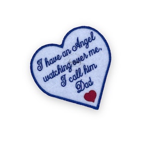 May include: A white heart-shaped patch with blue stitching around the edges. The patch has the text "I have an angel watching over me. I call him Dad" embroidered in blue thread. A small red heart is embroidered in the bottom right corner.