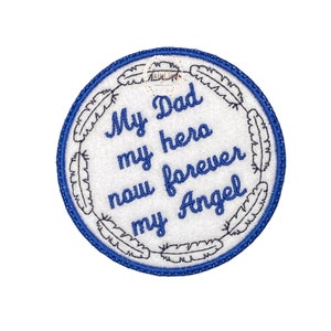 Op de afbeelding: Een witte cirkel met een blauwe rand en een verenontwerp rond de rand. De tekst in de cirkel luidt: "My Dad my hero now forever my Angel".