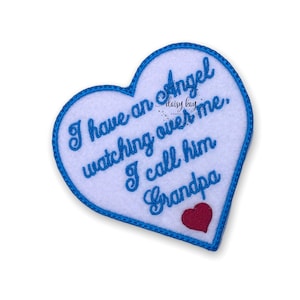 May include: A white heart-shaped felt patch with blue stitching around the edges. The patch has blue embroidered text that reads "I have an angel watching over me, I call him Grandpa". A small red heart is embroidered at the bottom of the patch.