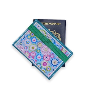 May include: A teal passport holder with a floral pattern and a green elastic band. The holder is sitting on top of a blue passport that says "British Passport".