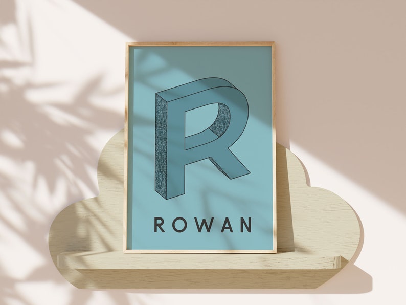 May include: A framed print with a blue background featuring a 3D stylized letter "R" in a darker blue color. The name "ROWAN" is printed in black below the letter.