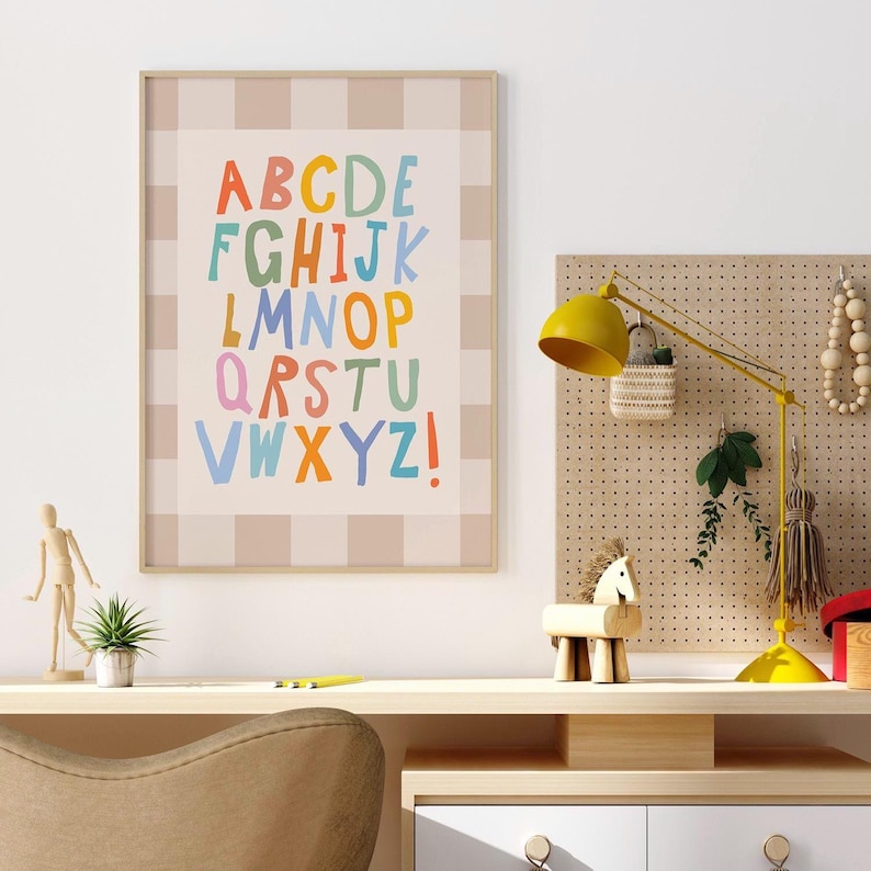 Puede incluir: Un cuadro de pared enmarcado que presenta el alfabeto con letras coloridas de estilo dibujado a mano sobre un fondo a cuadros de color beige claro y blanco. Las letras est&aacute;n dispuestas en filas, mostrando de la A a la Z en rojo, amarillo, verde y azul.
