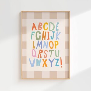 Puede incluir: Una l&aacute;mina decorativa enmarcada que muestra el alfabeto con una tipograf&iacute;a colorida de estilo manuscrito. Las letras se presentan en filas sobre un fondo crema, rodeadas por un borde a cuadros beige claro y blanco en un marco de madera.