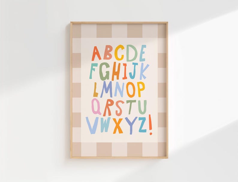 Puede incluir: Una l&aacute;mina decorativa enmarcada que muestra el alfabeto con una tipograf&iacute;a colorida de estilo manuscrito. Las letras se presentan en filas sobre un fondo crema, rodeadas por un borde a cuadros beige claro y blanco en un marco de madera.