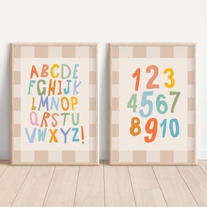 Puede incluir: Dos láminas enmarcadas con un borde a cuadros beige y blanco. Una lámina muestra el alfabeto en letras coloridas. La otra lámina muestra los números del 1 al 10 en varios colores. Las láminas están sobre un fondo beige claro.