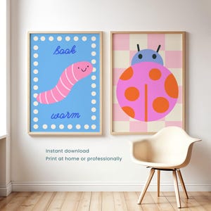 May include: Two framed wall art prints. The left print features a pink worm on a blue background with white dots and the text book worm. The right print displays a pink ladybug with orange spots on a pink and cream checkered background.