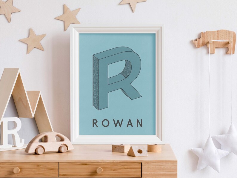 May include: A blue and white framed print with a large, 3D, blue letter "R" and the name "ROWAN" printed below it. The print is on a light blue background.
