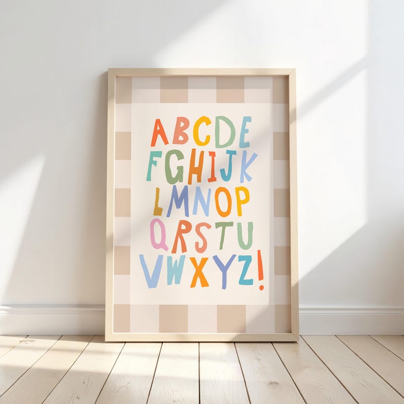 Puede incluir: Una l&aacute;mina de arte mural enmarcada que muestra el alfabeto con letras coloridas de estilo manuscrito dispuestas en filas. El fondo de la l&aacute;mina tiene un patr&oacute;n de cuadros en beige claro y blanco, con letras en tonos naranja, azul, verde y rosa.