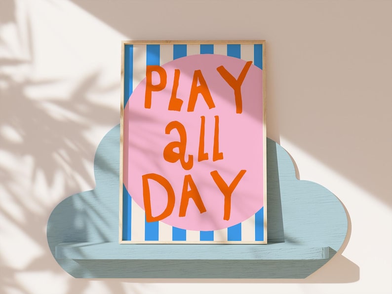 May include: A framed art print with the words "PLAY ALL DAY" in orange on a pink circle, set against a background of blue and white stripes. The artwork is displayed on a light blue cloud-shaped shelf.