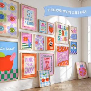 May include: A collection of colorful wall art prints in wooden frames featuring various illustrations including flowers, a strawberry, a bee, a rainbow, and text such as You Are One Of A Kind, Hello Sunshine, and Stay Silly. A blue banner reads 24 DESIGNS IN FIVE SIZES EACH.