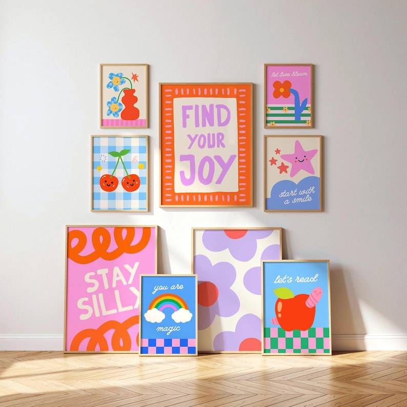 May include: A gallery wall of eight framed art prints featuring colorful illustrations of flowers, cherries, a rainbow, an apple, and stars. The prints include text such as FIND YOUR JOY, STAY SILLY, you are magic, let's read, and start with a smile.