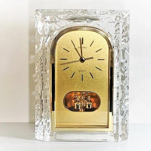 May include: A rectangular Seiko quartz clock with a gold-colored face and a clear, textured glass frame. The clock face has black hour markers and hands. The words "SEIKO" and "QUARTZ" are visible on the face.
