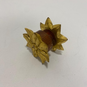 May include: A decorative wooden bottle stopper with a gold-colored floral design. The stopper has a dark brown wooden base and is adorned with two gold-colored, star-shaped floral embellishments on each end.