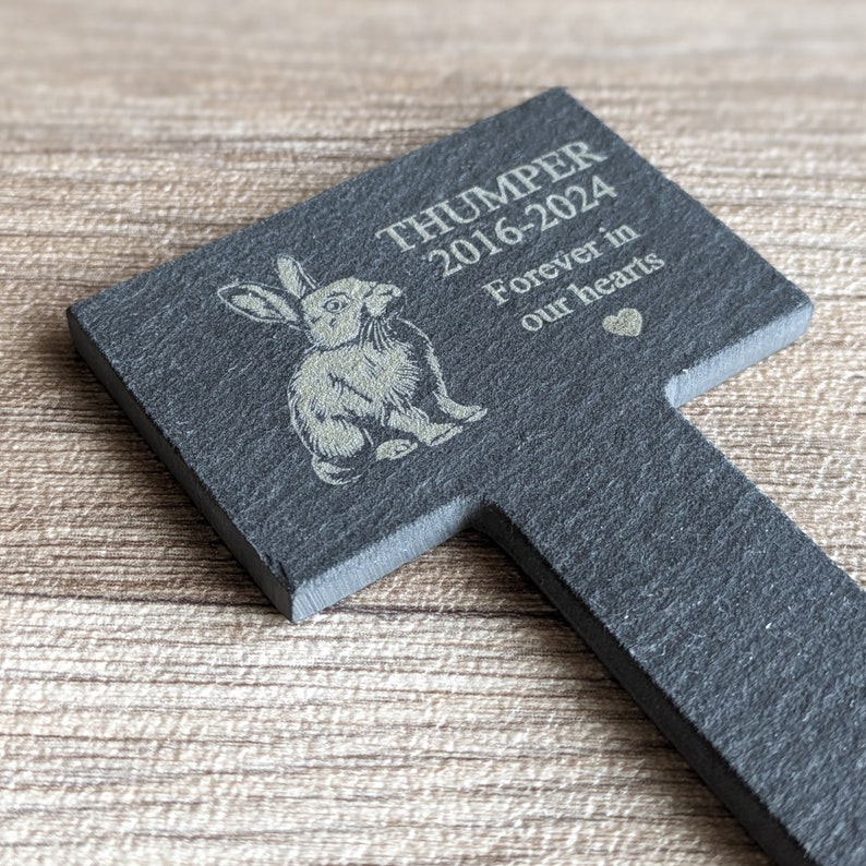 Puede incluir: Un marcador de jard&iacute;n de pizarra negra con una silueta de conejo blanco y la inscripci&oacute;n "THUMPER 2016-2024 Forever in our hearts".
