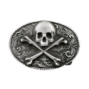 May include: Silver belt buckle with a skull and crossbones design. The skull is detailed with eye sockets, a nose, and a mouth. The crossbones are made of two long bones that intersect in the middle. The buckle is surrounded by a decorative border.