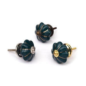May include: Three dark teal pumpkin-shaped cabinet knobs with gold-colored vertical stripes. Each knob features a metallic center accent and a threaded metal bolt extending from the back for installation on furniture or cabinetry doors.