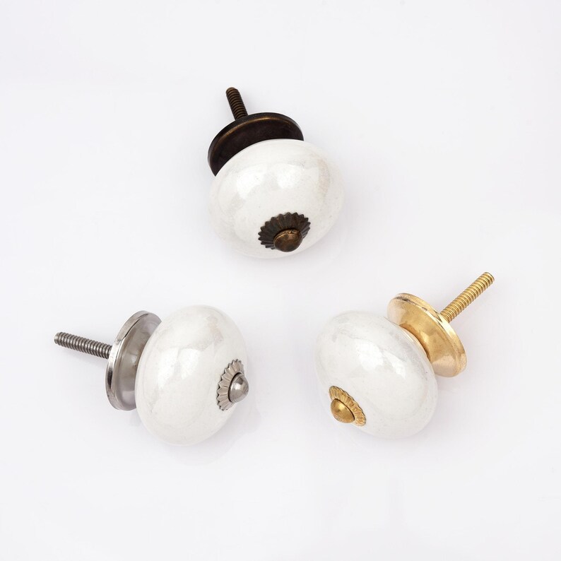 Peut inclure: Trois boutons de placard ronds en c&eacute;ramique blanche avec une finition brillante. Chaque bouton pr&eacute;sente un accent m&eacute;tallique central et une tige filet&eacute;e. Les bases sont finies dans des tons bronze fonc&eacute;, argent bross&eacute; et or poli.