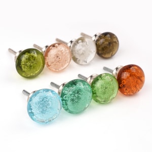Puede incluir: Una colección de ocho pomos de cristal de colores. Los pomos son redondos con una textura similar a burbujas y vienen en tonos de azul, verde, naranja y marrón. Cada pomo tiene un vástago metálico plateado para el montaje.