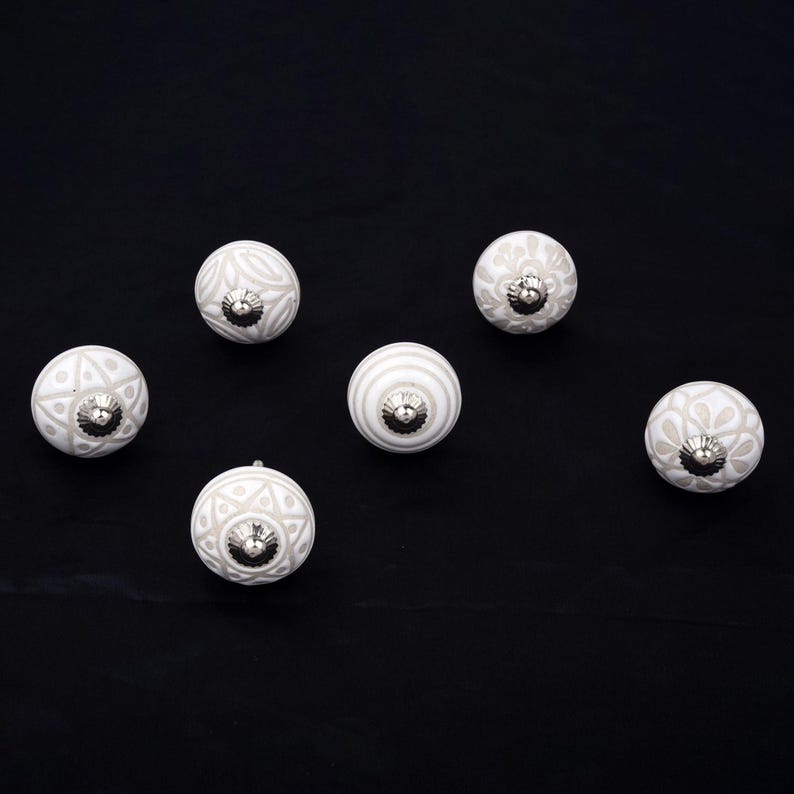Op de afbeelding: Een set van zes ronde kastknoppen met witte en lichtgrijze patronen. Elke knop heeft een bolvorm met een zilverkleurige metalen kern. De ontwerpen bevatten diverse geometrische en florale motieven die op het oppervlak zijn gedrukt.