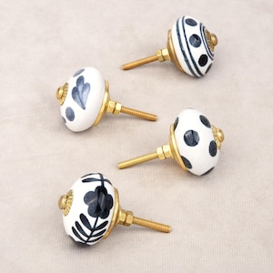 Peut inclure: Quatre boutons de meuble en céramique blanche avec des fixations en laiton. Chaque bouton présente un motif noir et bleu différent, comme des pois, des rayures et des motifs floraux. Idéal pour décorer les meubles.