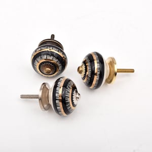 May include: Three round cabinet knobs featuring a black and white striped pattern with gold-toned metallic bands and a central decorative metal cap. Each knob includes a threaded metal screw post extending from the back for mounting purposes.