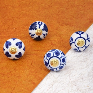 Peut inclure: Quatre boutons de meuble décoratifs en céramique. Chaque bouton rond est blanc avec un motif floral bleu et une base en métal doré. Les motifs floraux varient.