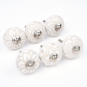 Puede incluir: Conjunto de siete pomos de cerámica blanca para armarios con diseño floral en color beige claro. Cada pomo tiene una base y un tornillo de metal plateado. Estos pomos decorativos son ideales para renovar muebles.