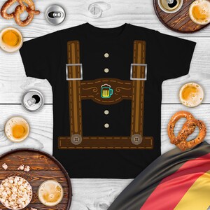 May include: Black t-shirt with a brown and white graphic of lederhosen suspenders and a beer stein. The graphic has a stitched look and includes three buttons.