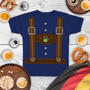 May include: A navy blue t-shirt with a brown leather lederhosen design. The design features a beer stein and stitching details.