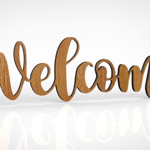 Puede incluir: Letrero de madera "Bienvenido" en fuente cursiva. El letrero es de madera marrón claro con veta visible. La palabra está recortada y se apoya sobre una superficie blanca, con un reflejo visible debajo.